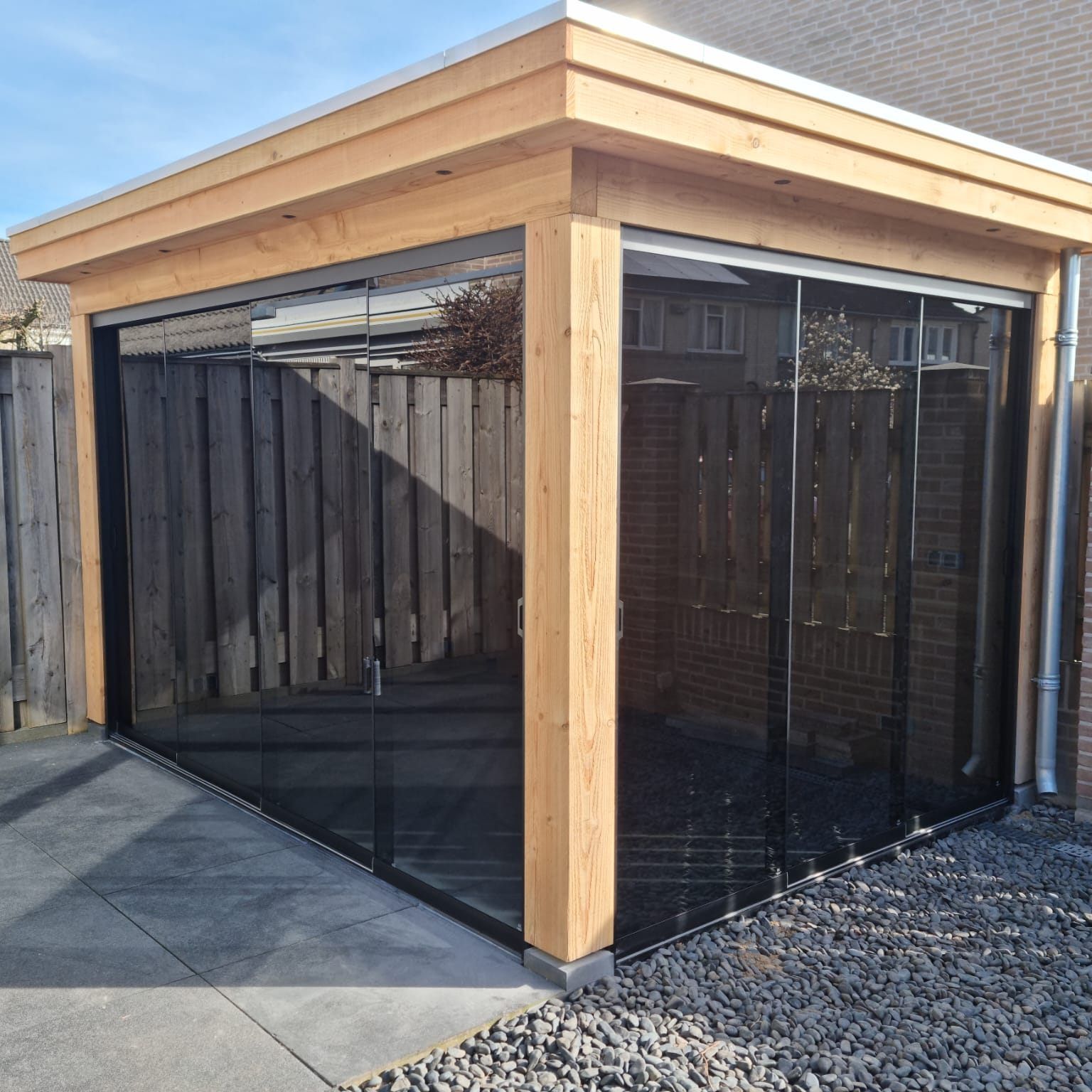 Een houten constructie met glazen schuifdeuren en een hek op de achtergrond