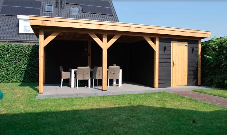 Een houten tuinpaviljoen met een open zitgedeelte, zwarte gevelbekleding, een deur en een tafel met stoelen op een terras.