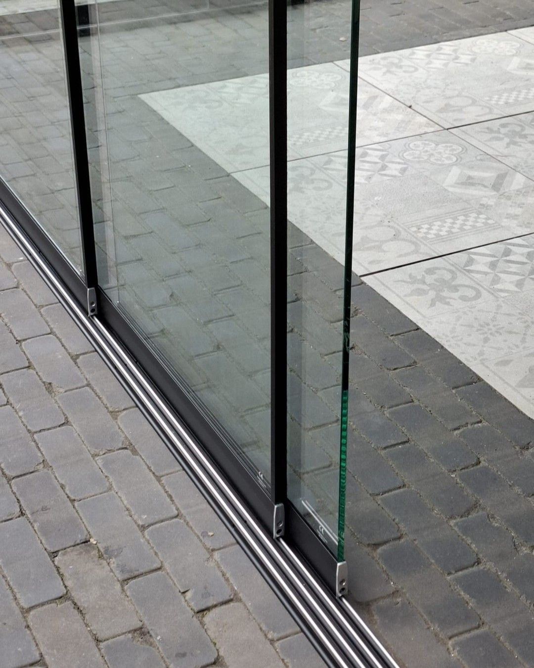 Een close-up van een meerdelig metalen schuifdeursysteem, geïnstalleerd op een bakstenen terras.