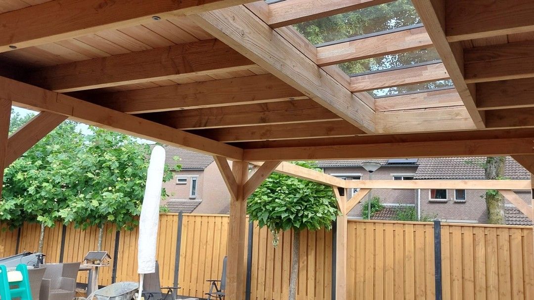Een houten pergola met een transparant dak in een achtertuin.