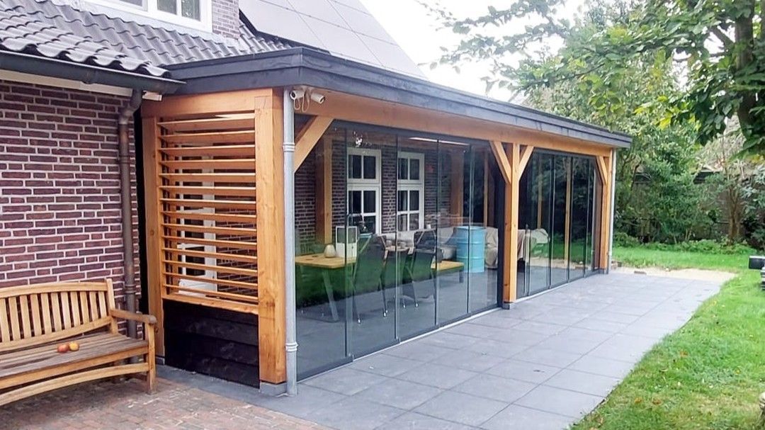 Een houten veranda met glazen schuifdeuren bevindt zich naast een bakstenen gebouw.