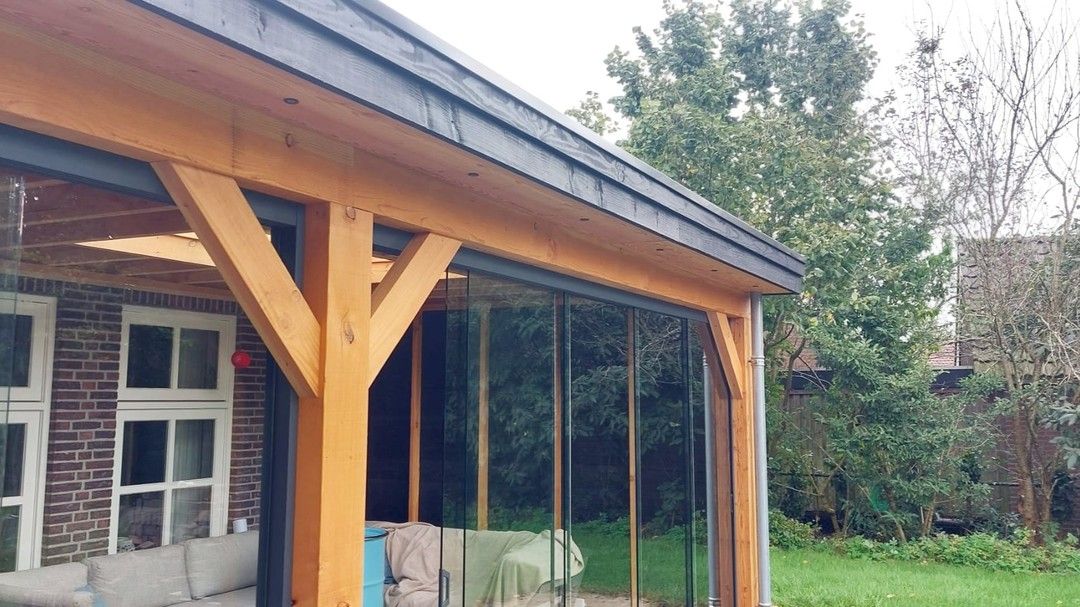 Een houten veranda met glazen schuifdeuren en een bakstenen gebouw op de achtergrond.