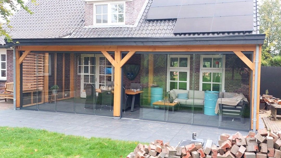 Voor een huis staat een houten veranda met glazen schuifdeuren.