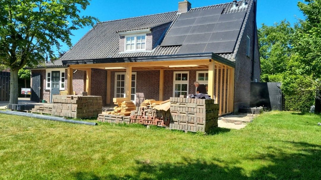 Een huis met een veranda en zonnepanelen op het dak staat op een weelderig groen veld.
