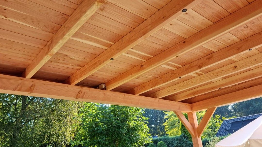 Het plafond van een houten constructie met bomen op de achtergrond.