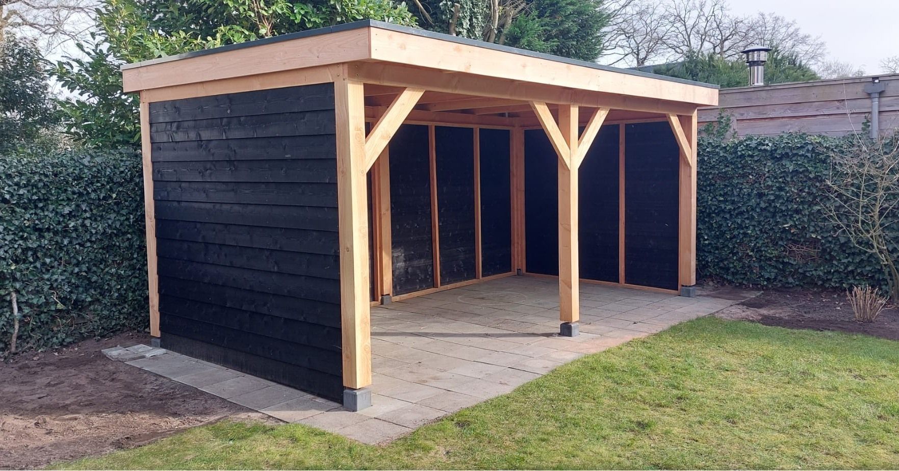 Een houten schuur staat midden in een weelderige groene tuin.