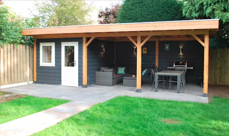 Een tuinhuisje in de achtertuin met een donkergrijze, afgesloten ruimte met een witte deur en een aangrenzend openluchtterras met zitgelegenheid.