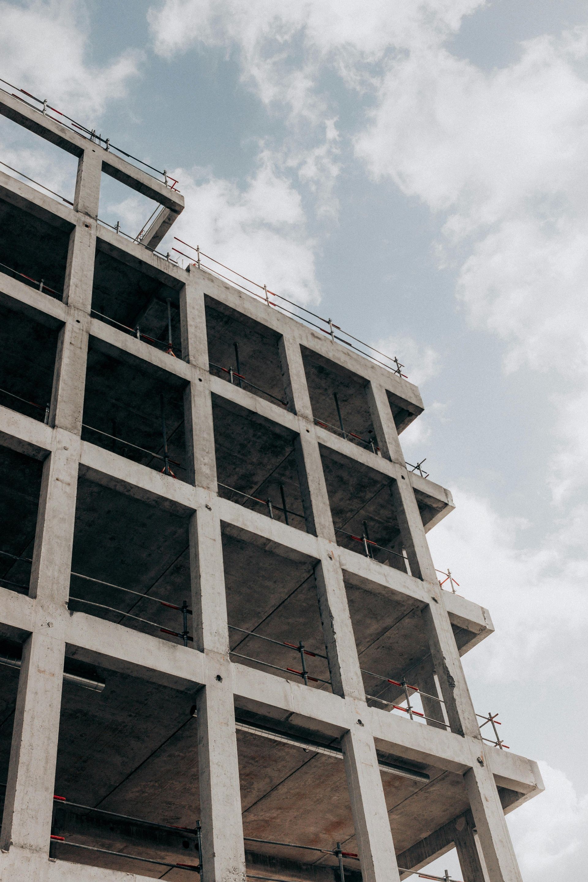 Laag perspectief van het skelet van een meerlaags betonnen gebouw onder een bewolkte hemel.