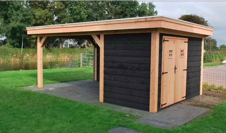 Een houten tuinconstructie met een zwart schuurtje en een open, overdekt zitgedeelte op een grasveld.