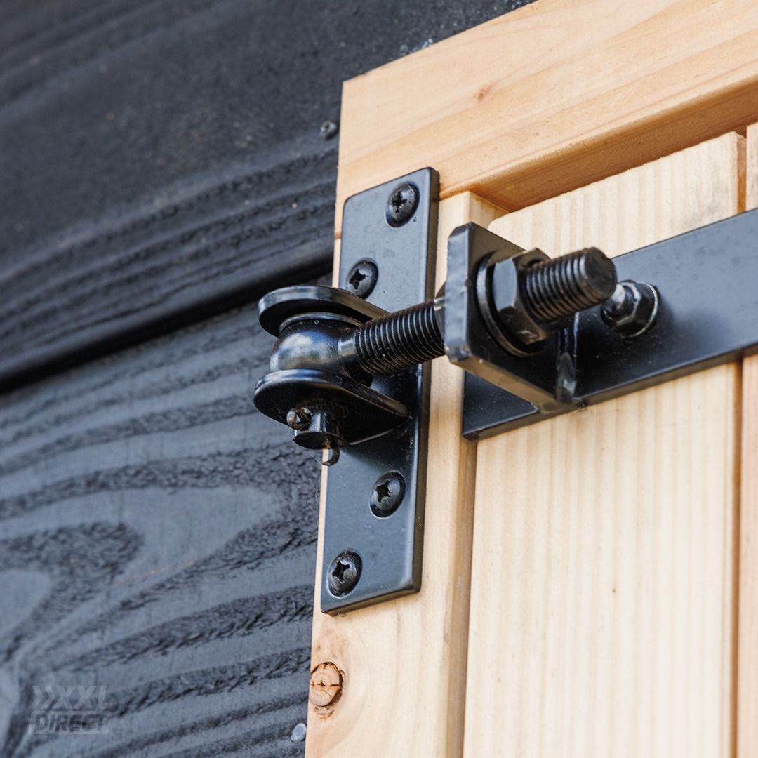 Een zwart metalen scharnier is gemonteerd op een houten luik en een donker geverfde buitenmuur, waardoor het luik open kan zwaaien.