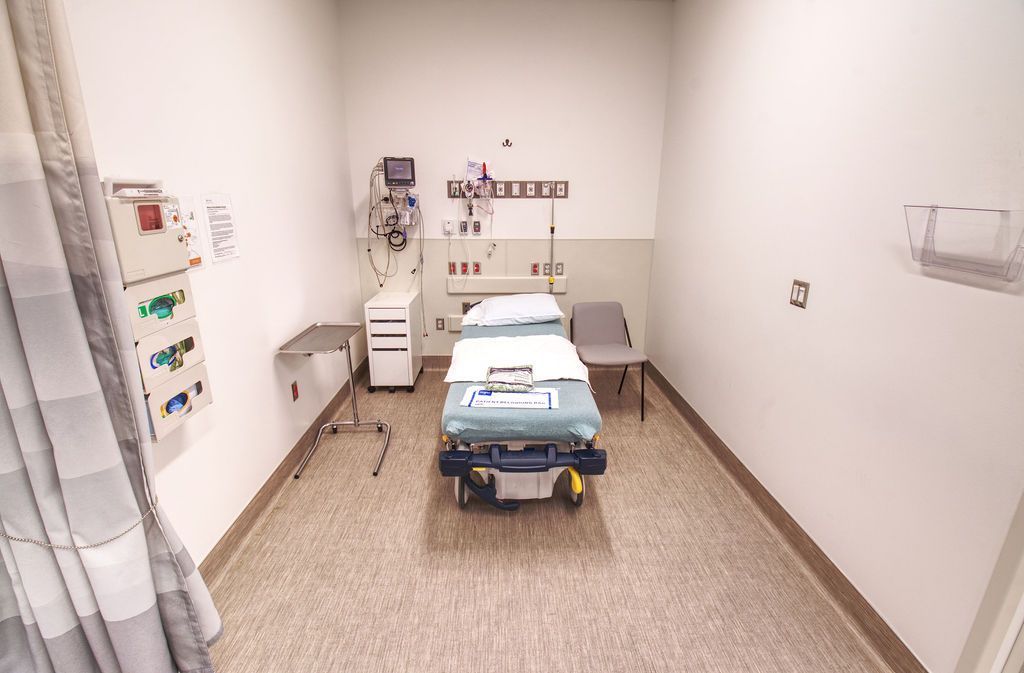 image of an emergency room cubicle with a bed in the middle surrounded by hospital equipments and a chair.