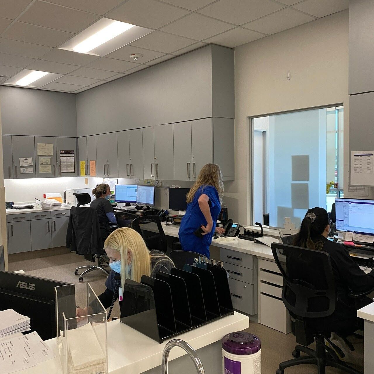 image of nurse's and staff in the office on their computer wearing a face-masks surrounded by office supplies