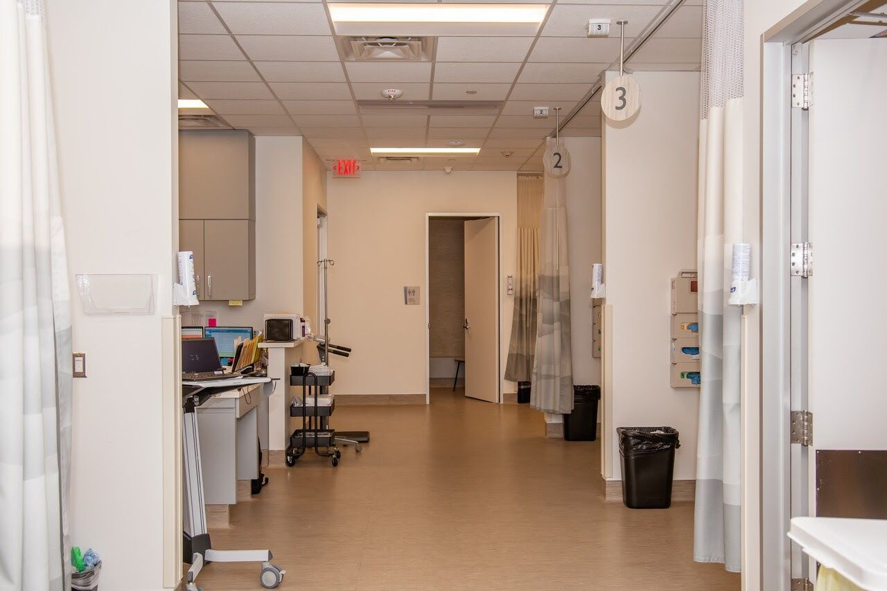 image of a hallway with cubicles with hospital beds on both sides and a nurse station on the left.