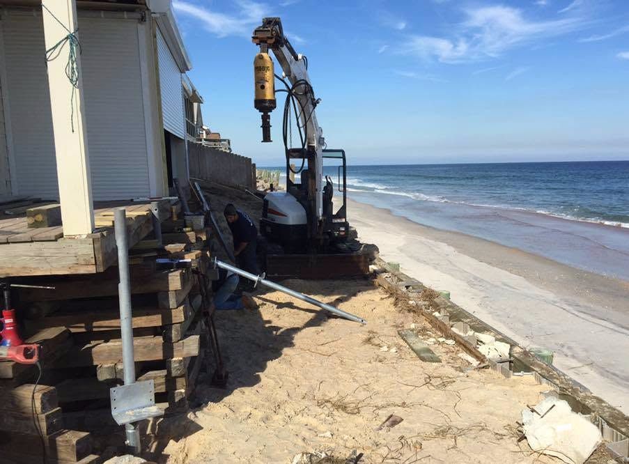 Beach erosion repair equipment beside a house on a sandy shoreline under a blue sky