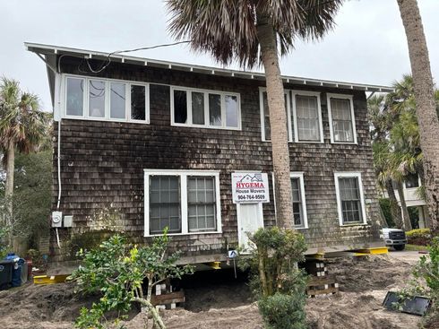 Two-story weathered house with a palm tree and a yard sign in front
