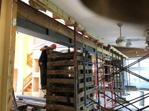 Construction site with stacked pallets, scaffolding, and a worker on the left side indoors