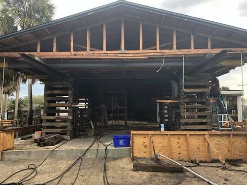 Open-sided wooden shed under construction with scaffolding, tools, and a dirt floor