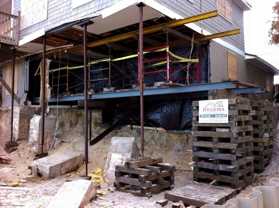 House under construction on stilts with scaffolding, brick stacks, and rubble on a sloped site