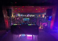 DJ booth in a dark nightclub with neon lights and a crowded dance floor beyond