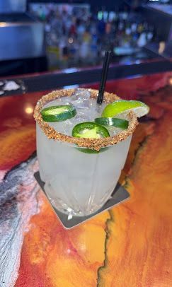 Salt-rimmed margarita with lime wedges and a straw on a bar top.