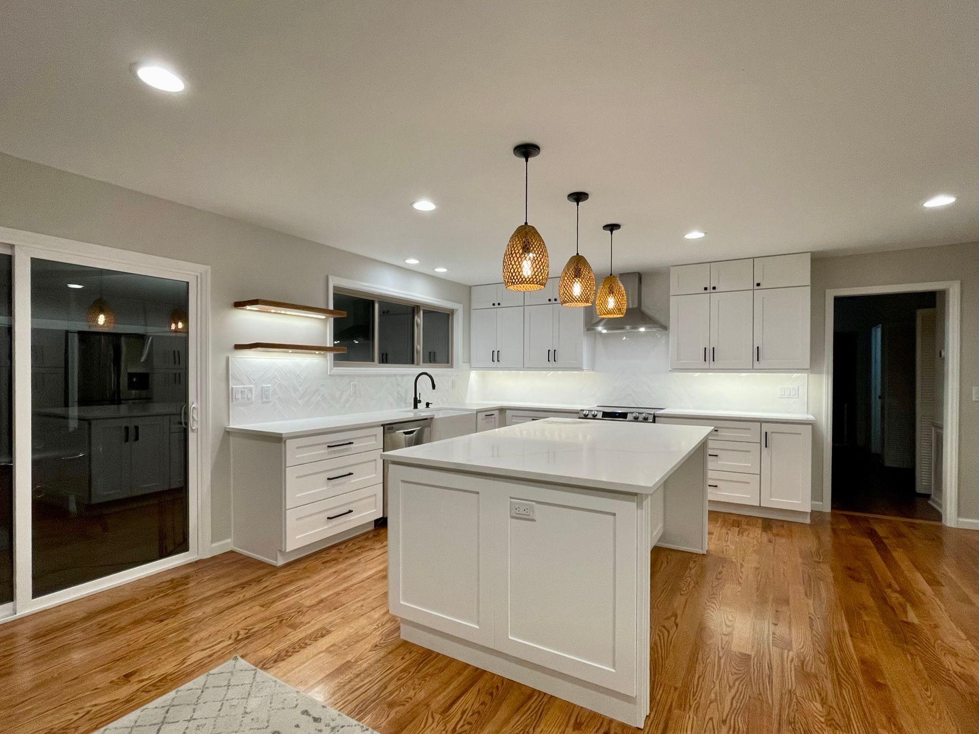 Modern white kitchen with island, pendant lights, and wood floors.