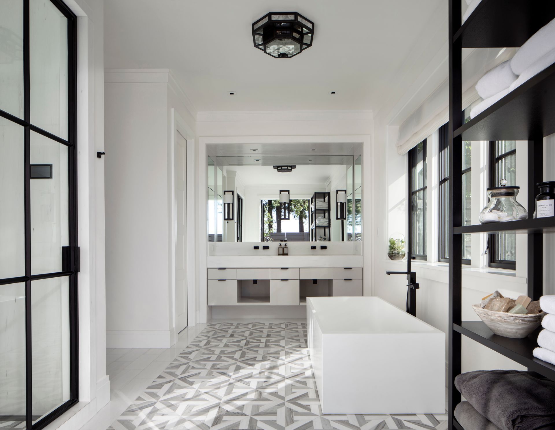 A bright, modern white bathroom featuring a freestanding tub, geometric tile floors, a double vanity, and black accents.