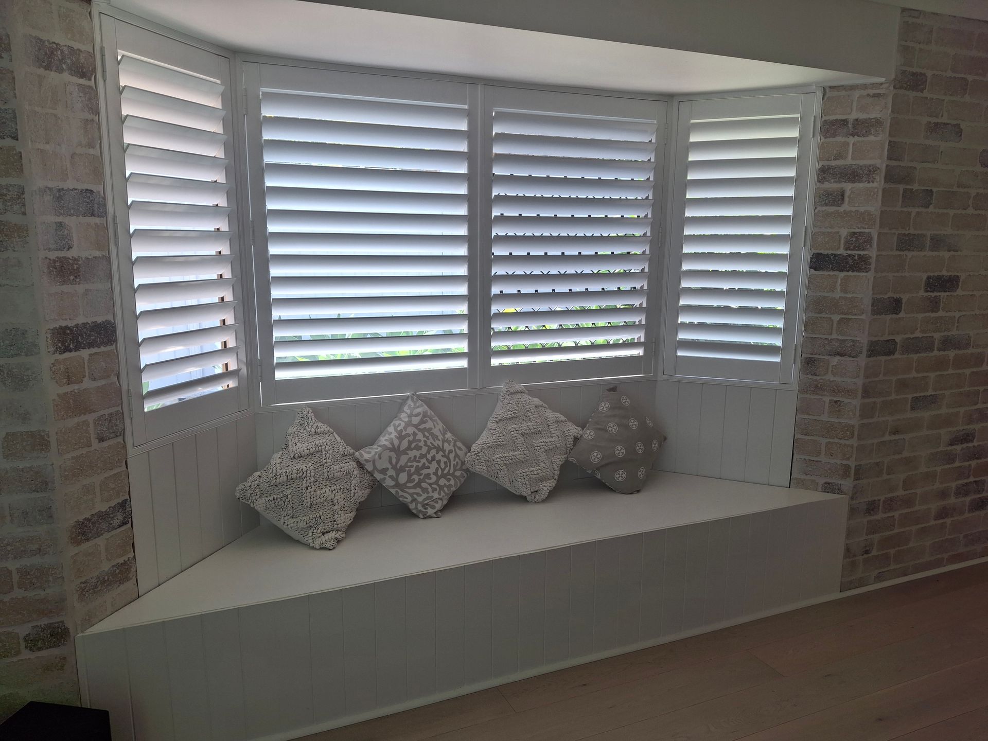 Window seat with white shutters and patterned cushions in a brick-lined alcove