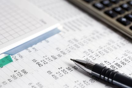 Pen on printed financial tables beside a calculator and notebook on a desk