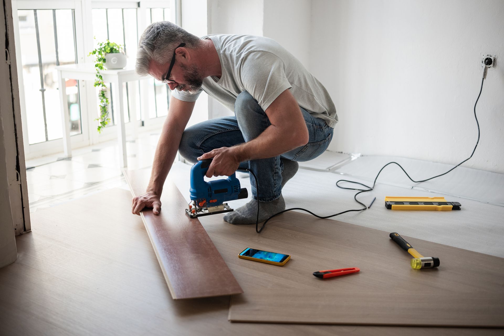 Carpenter cutting laminate floor plank using jigsaw, highlighting flooring services. Carpenter cutting laminate floor plank using jigsaw, highlighting flooring services.