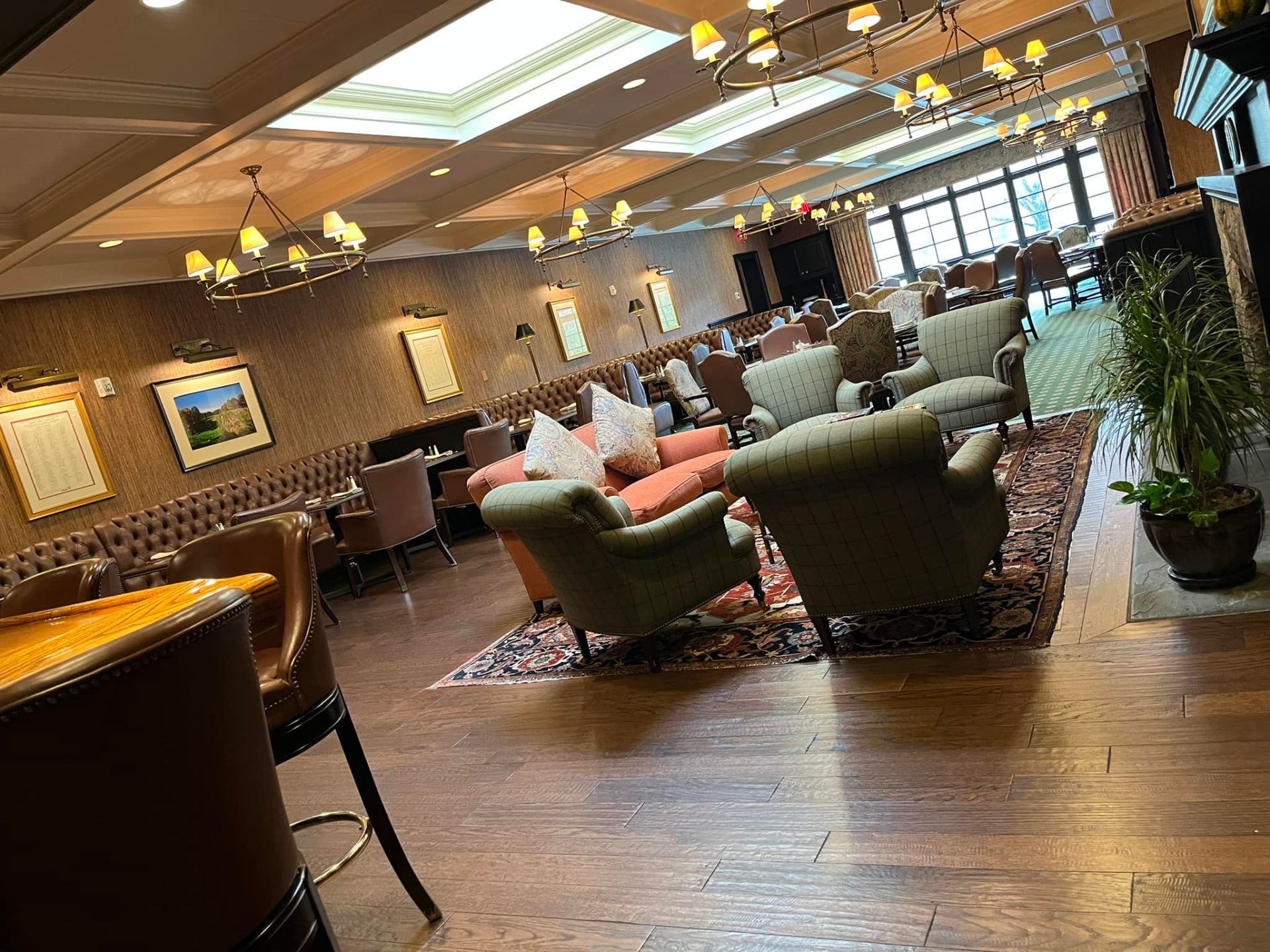 Lounge with armchairs, couches, and tables on a patterned rug; overhead chandeliers and natural light.