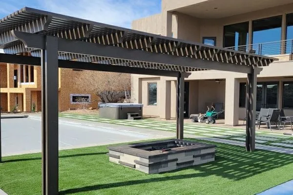 Modern backyard patio with a pergola, fire pit, and turf lawn beside a house