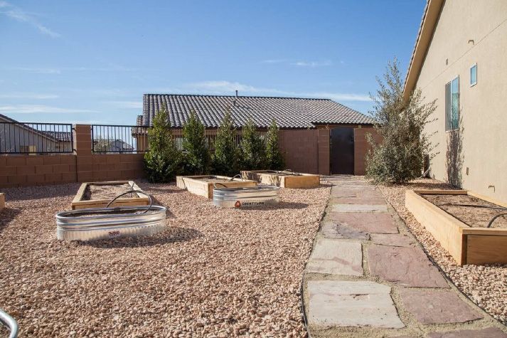 A walkway leading to a house with a lot of raised beds in the backyard.