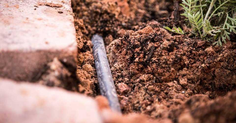 A close up of a pipe in the ground next to a brick wall.