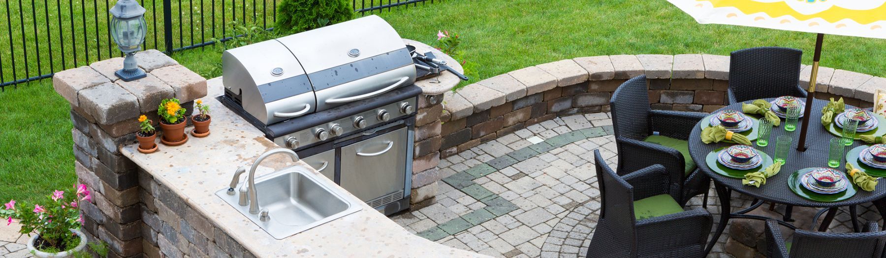 A patio with a grill , sink , table and chairs.