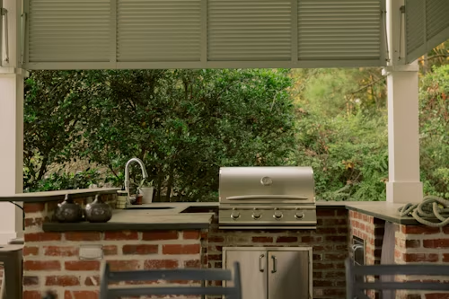 Outdoor kitchen with brick, stainless steel grill, and foliage backdrop.