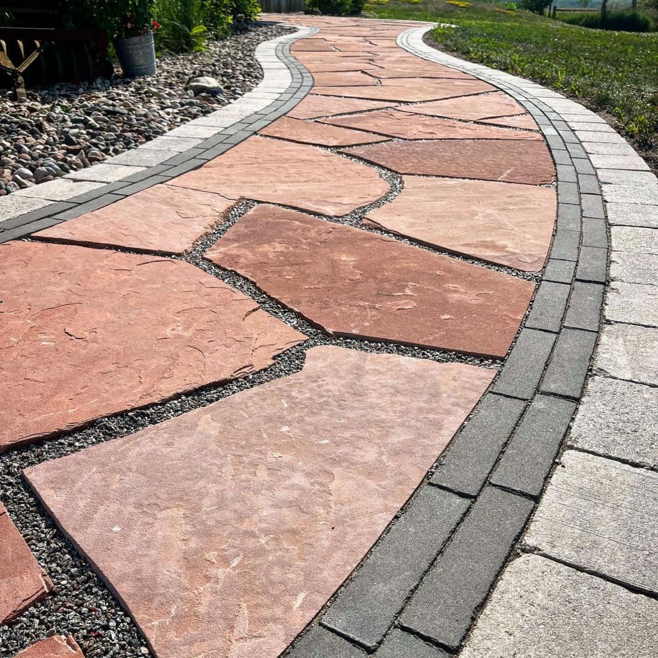 A stone walkway with a brick border is surrounded by grass and rocks.