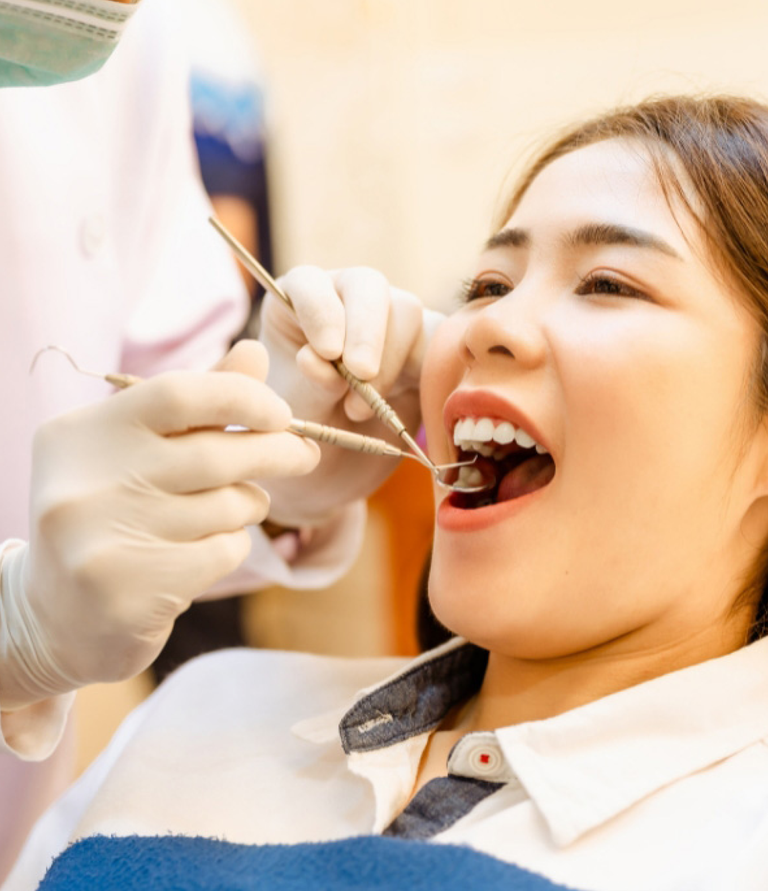 Person in dental chair, mouth open, dentist examining teeth with tools.