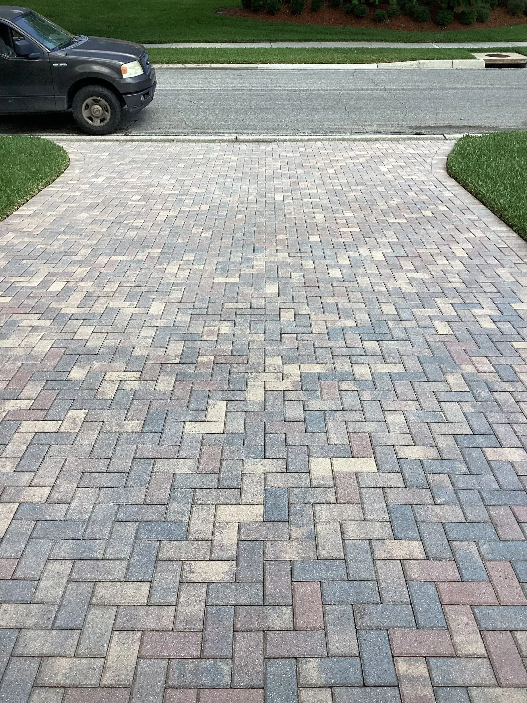 Brick-paved driveway leading to a street, with a black truck parked at the top left.