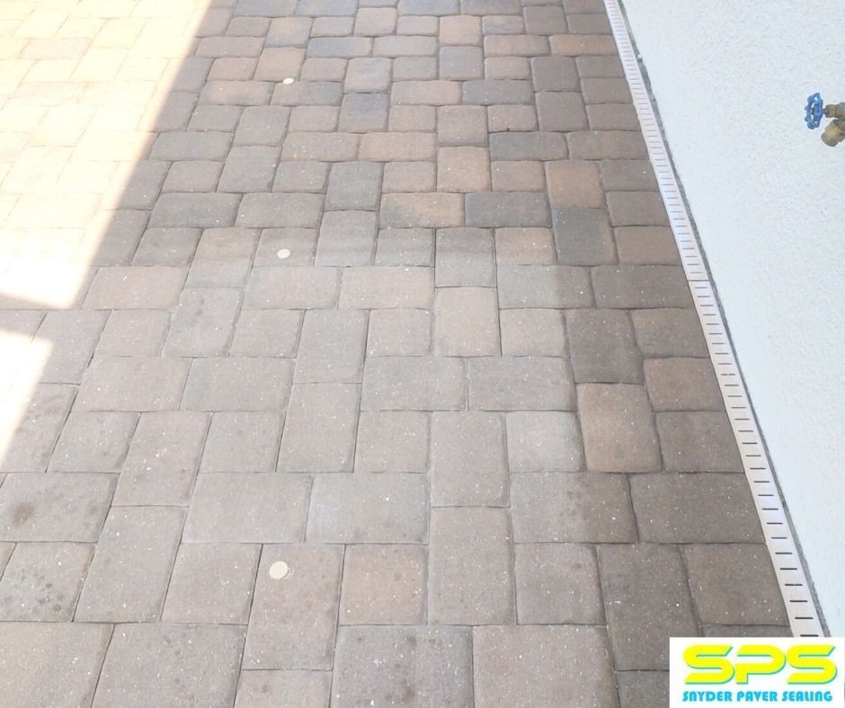 Stone paver walkway beside a white wall, with bright sunlight and shadows at the left edge.