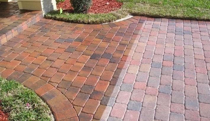 Curved brick walkway with reddish and brown pavers beside trimmed grass and garden mulch.