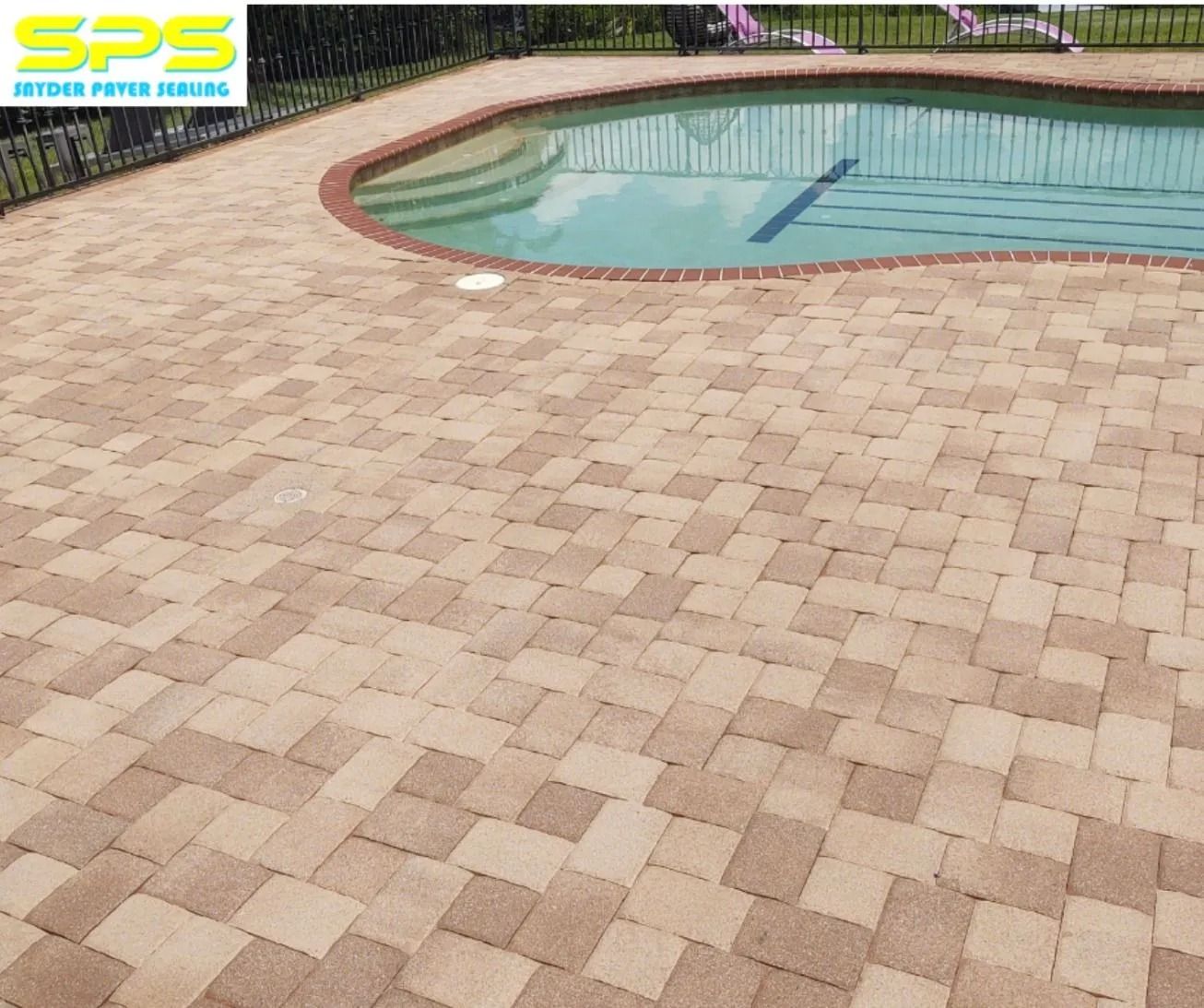 Tan brick paver patio surrounding a curved swimming pool with blue water