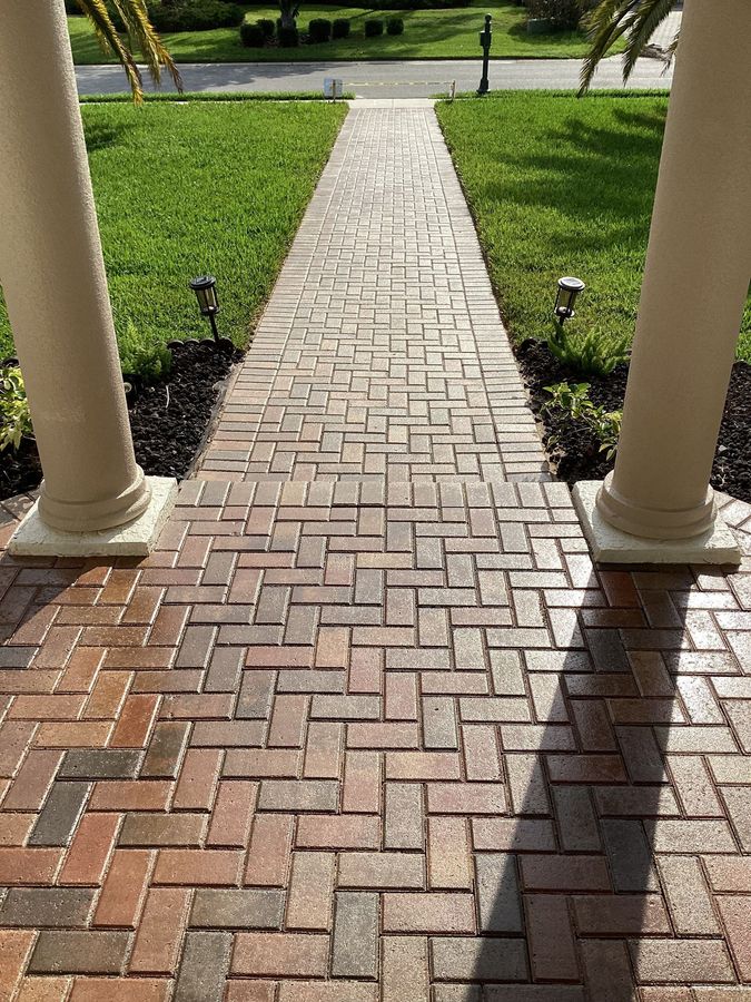 Brick walkway between porch columns leading to a sunlit green lawn and path beyond.