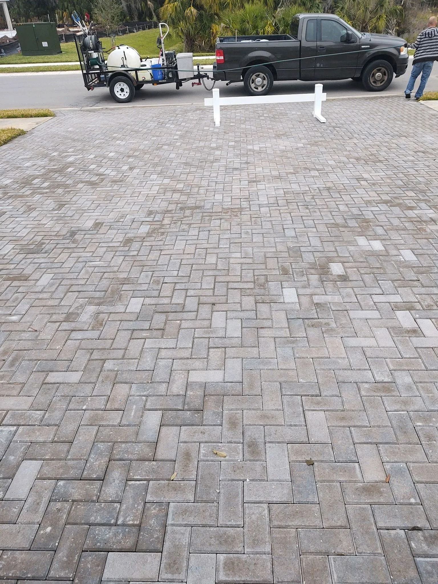 Brick driveway with a black pickup truck, trailer, and people near a white fence post outdoors