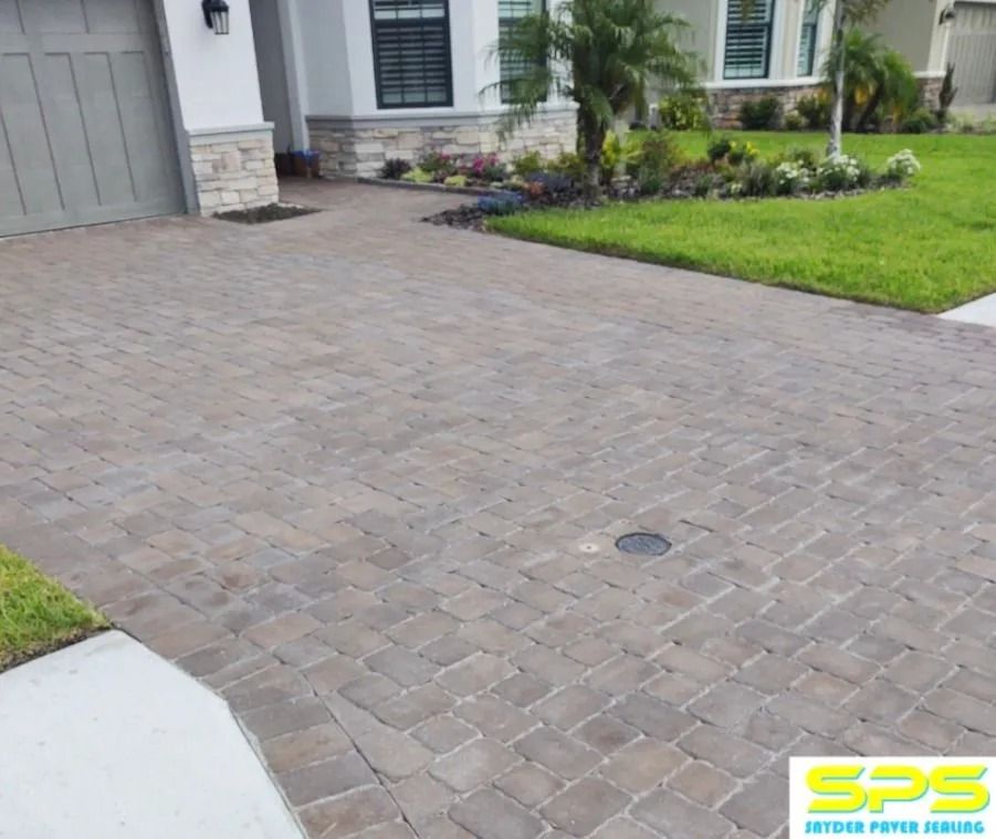 Brick driveway leading to a house entrance with a green lawn and shrubs