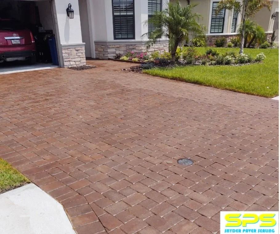 Brick driveway leading to a house with a garage, white columns, and green landscaping.