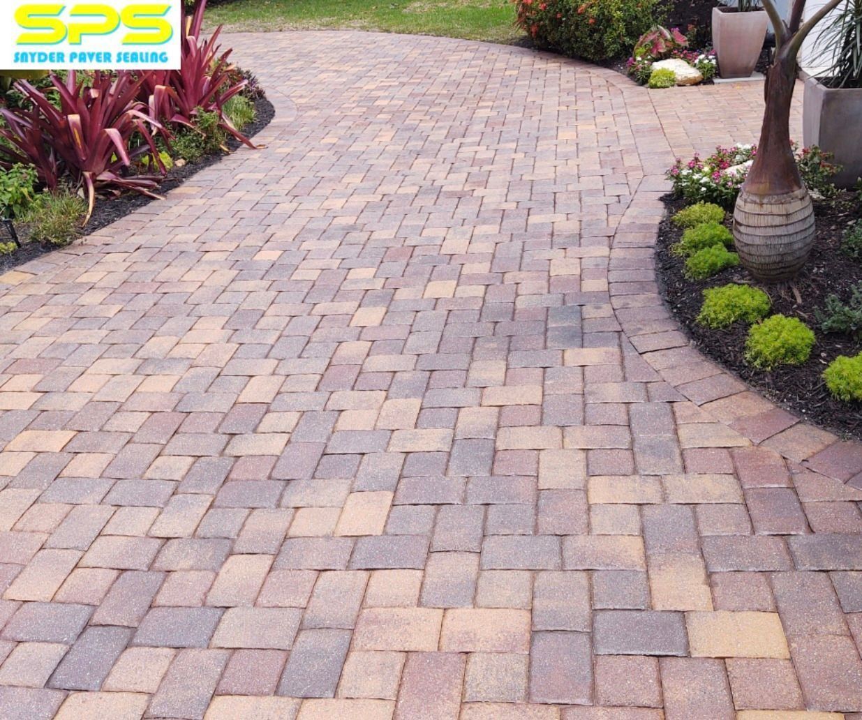 Curved brick paver driveway bordered by landscaping and palm trees