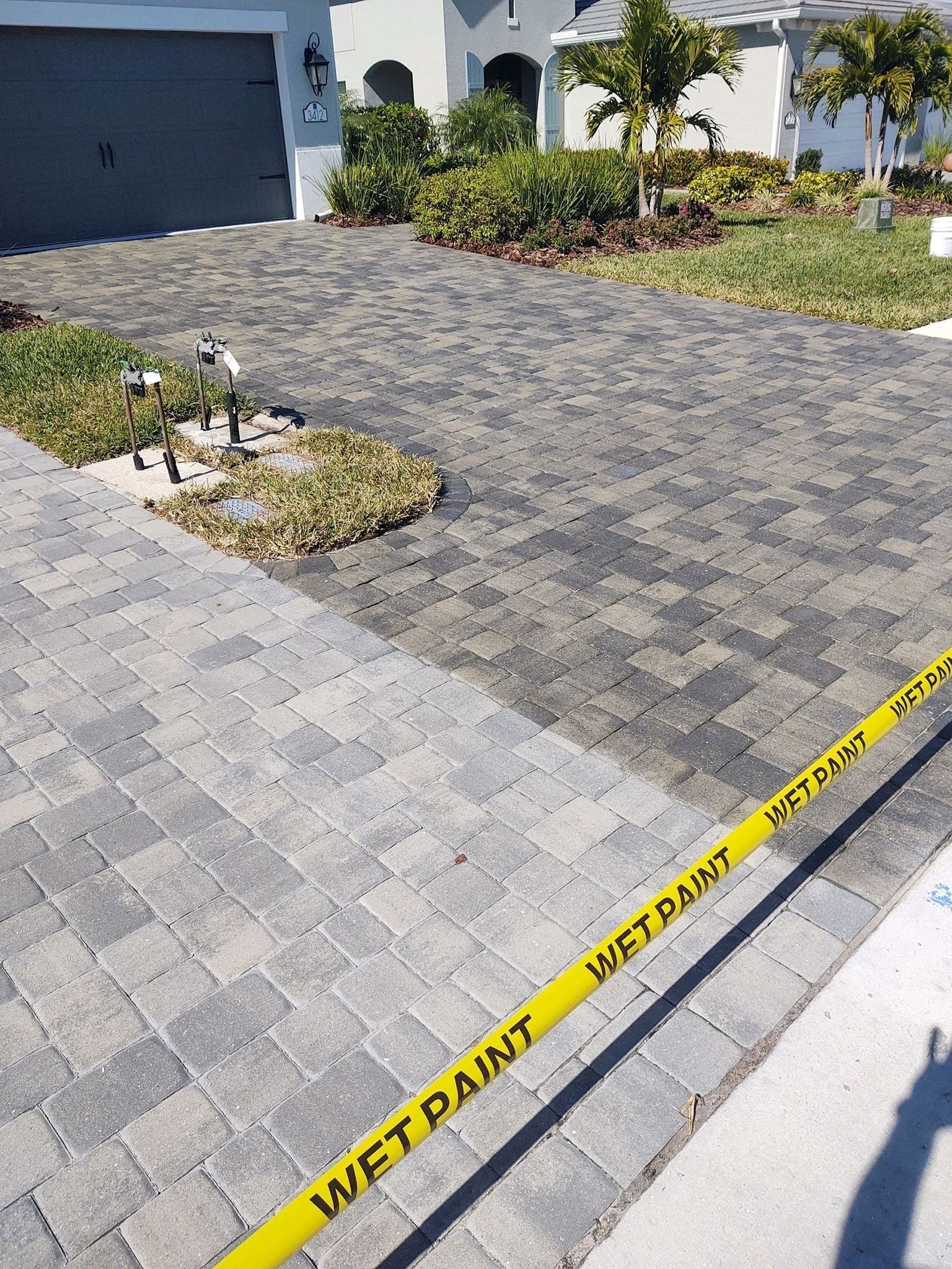 Caution tape across a gray paver driveway beside a garage and landscaped front yard