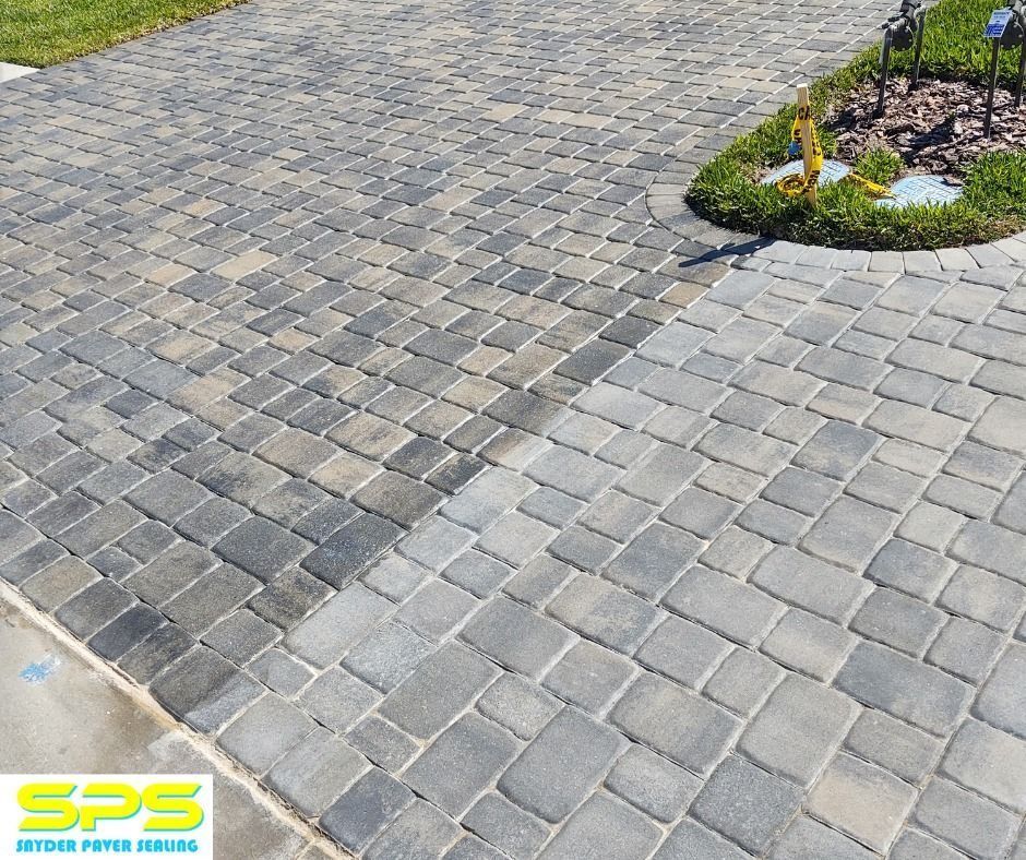 Gray and tan interlocking paver driveway with a curved garden border and SPS logo in the corner