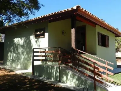 Casa amarela de estuque com persianas marrons, telhado de telha e rampa de acesso.
