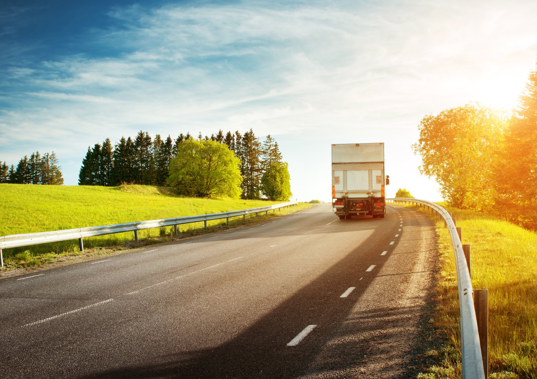 A white truck is driving down a country road.